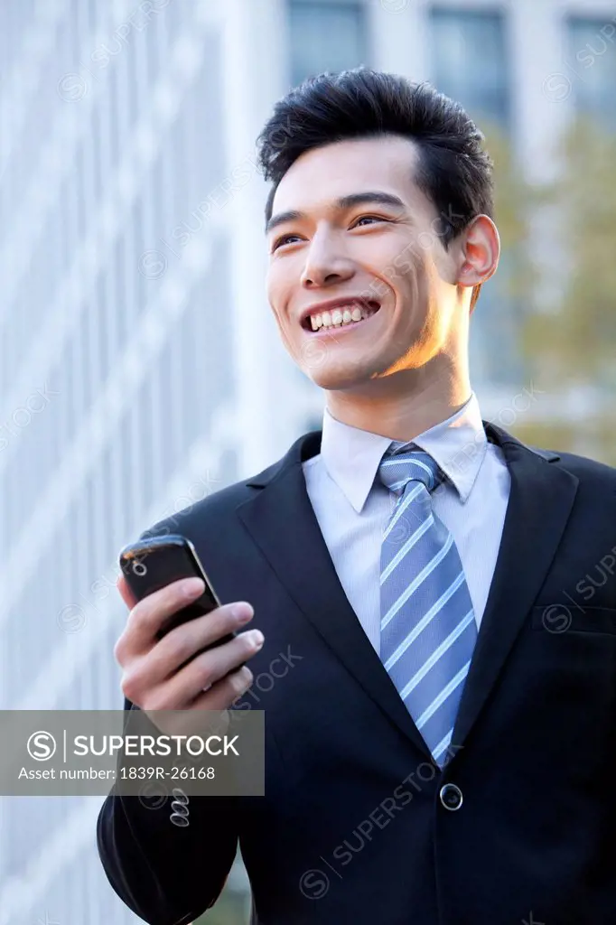 Businessman outside office buildings holding his mobile phone