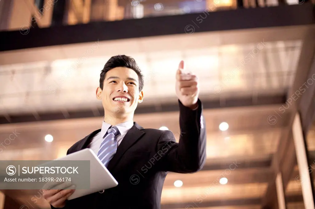 A businessman using a digital tablet and giving a thumbs up outside an office building at night
