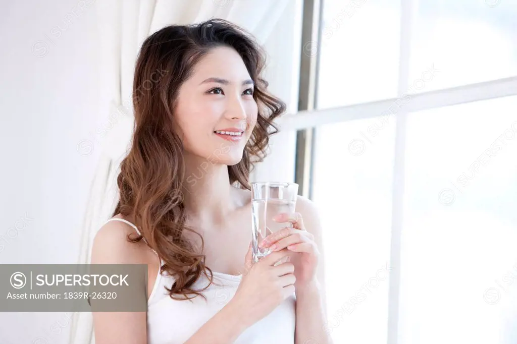 Young woman drinking water by window
