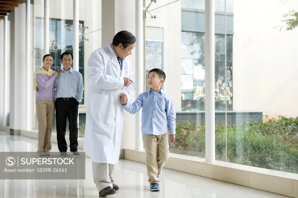 Young Family Walks in a Hospital Corridor With a Doctor