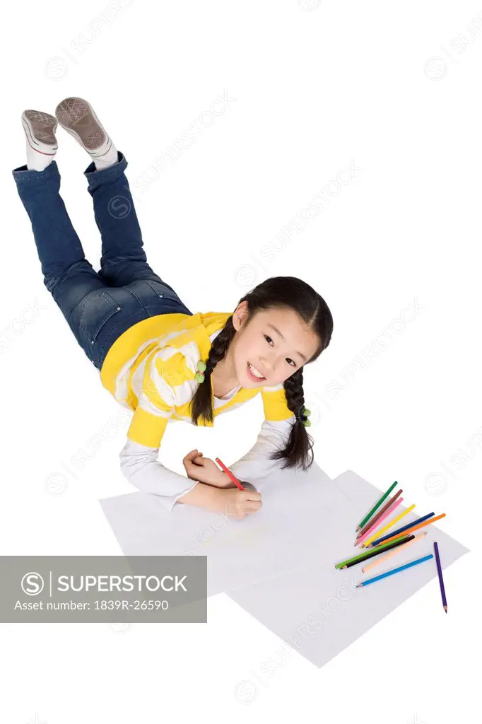 A young girl coloring while lying on the floor