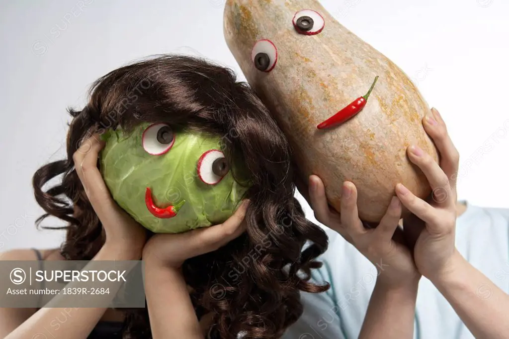 Two People Covering Their Faces With Masks Made Of Vegetables