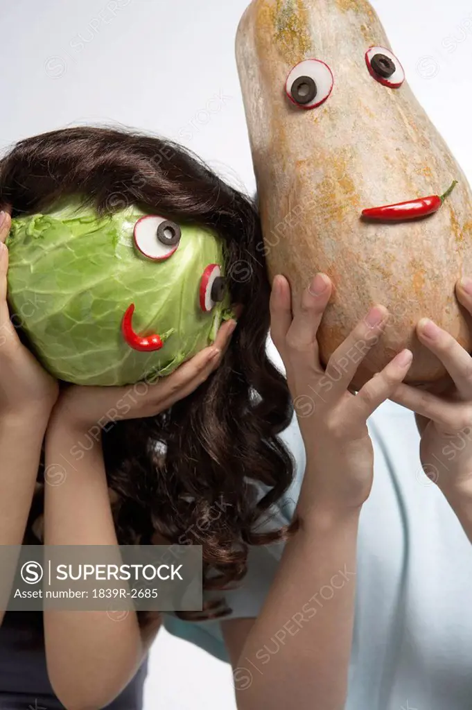 Two People Covering Their Faces With Masks Made Of Vegetables.