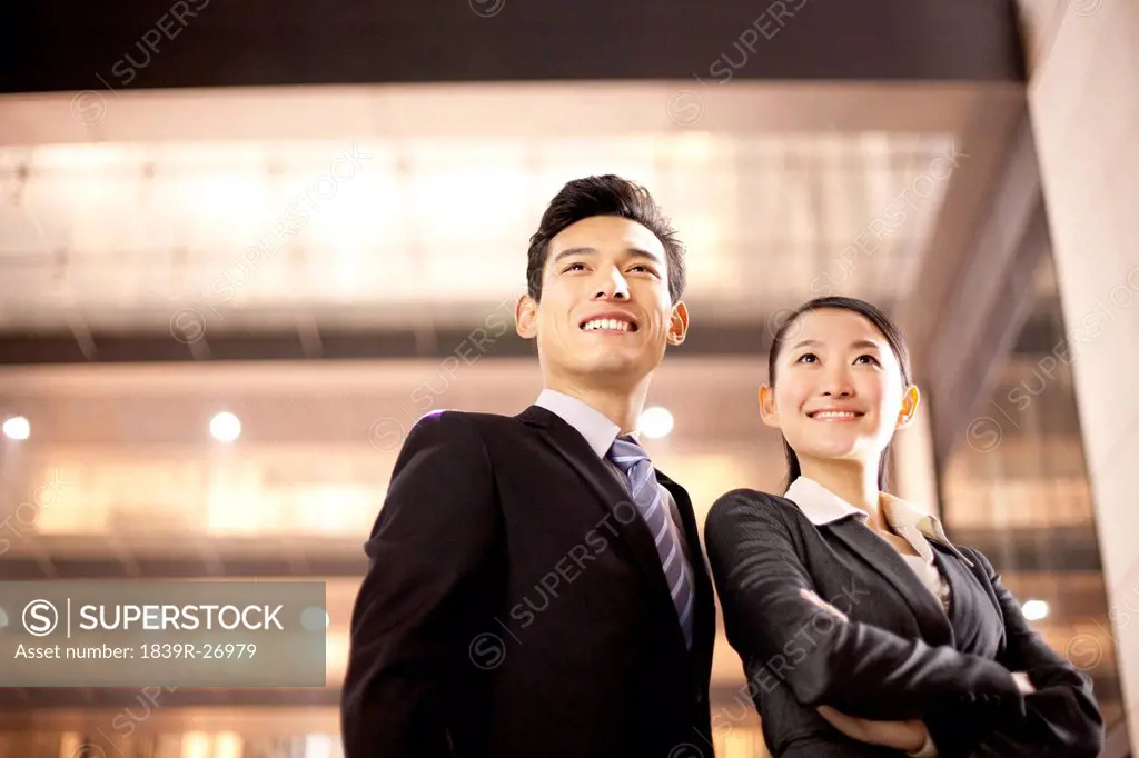 A businessman and businesswoman outside an office building at night