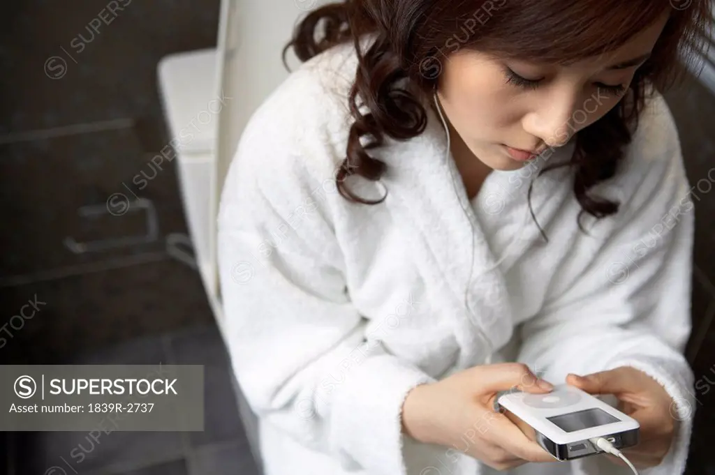 Young Woman Sitting On The Toilet Listening To Mp3 Player