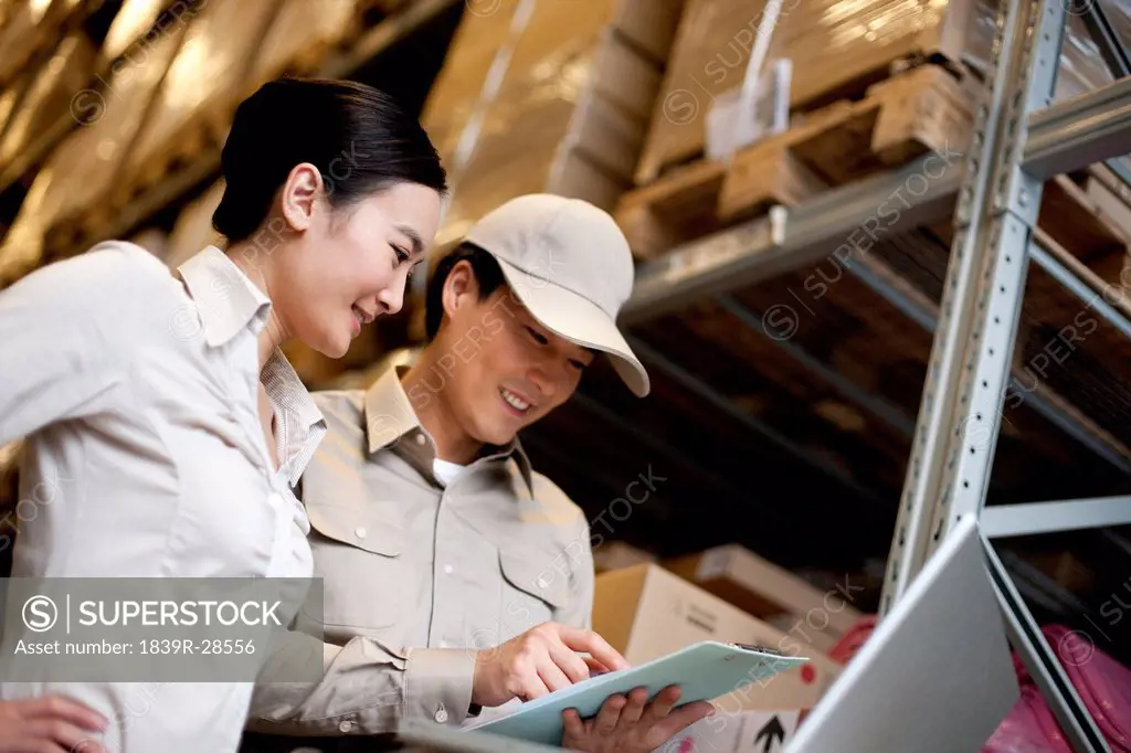 Chinese businesswoman in a warehouse with worker using a laptop