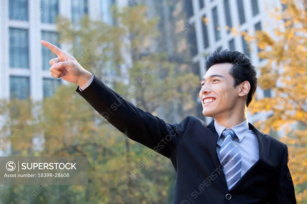 Businessman outside office buildings pointing to something