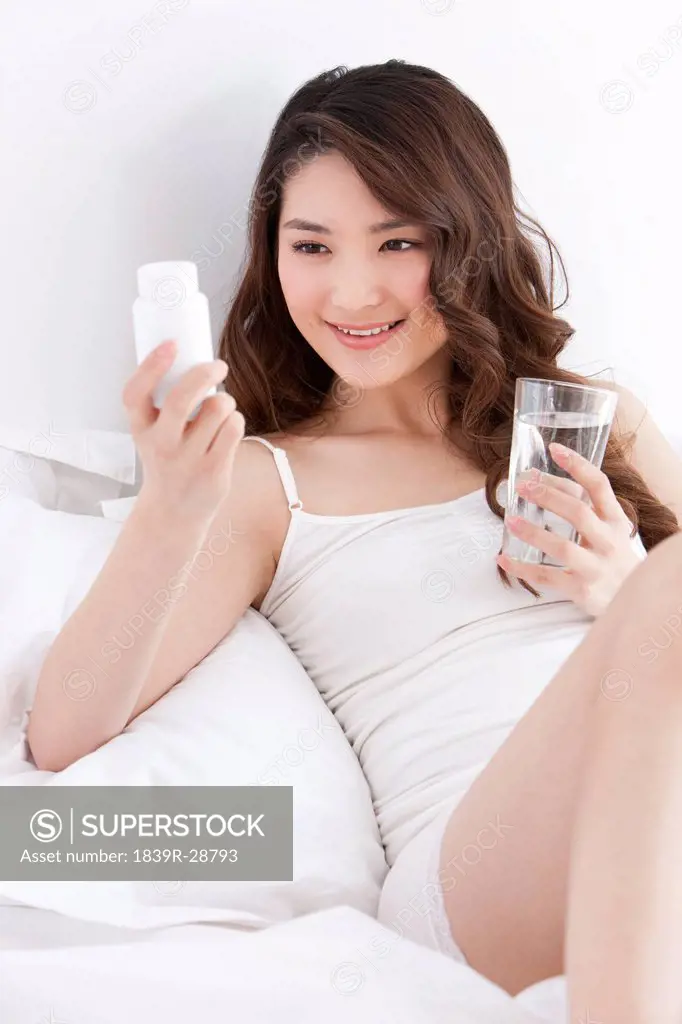 Young woman taking medicine in bed