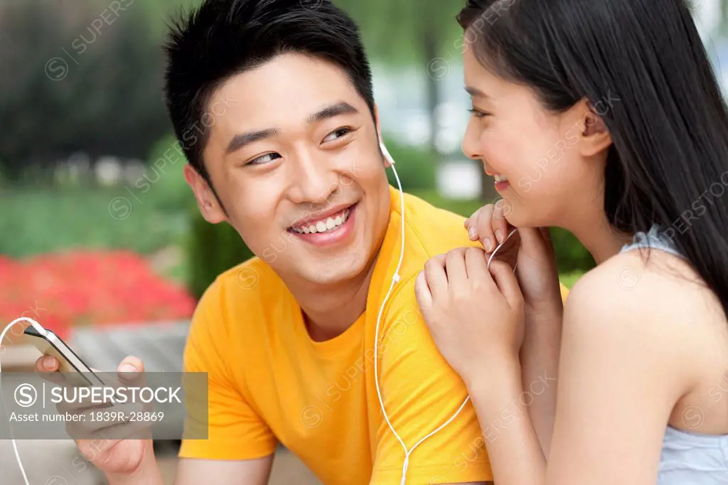 Young couple listening to music on mobile phone outdoors
