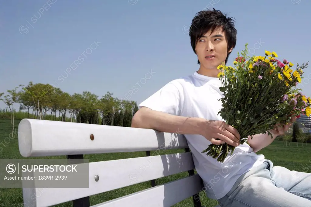 Young Man Sitting On A Park Bench Holding Flowers