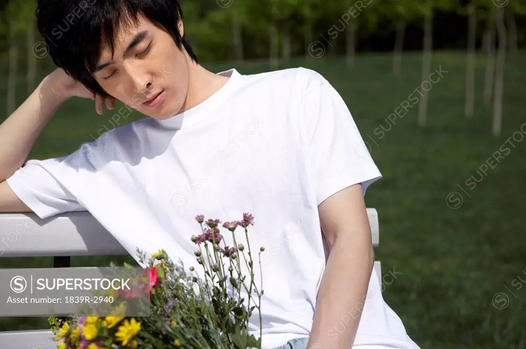 Young Man Sitting On A Park Bench Holding Flowers