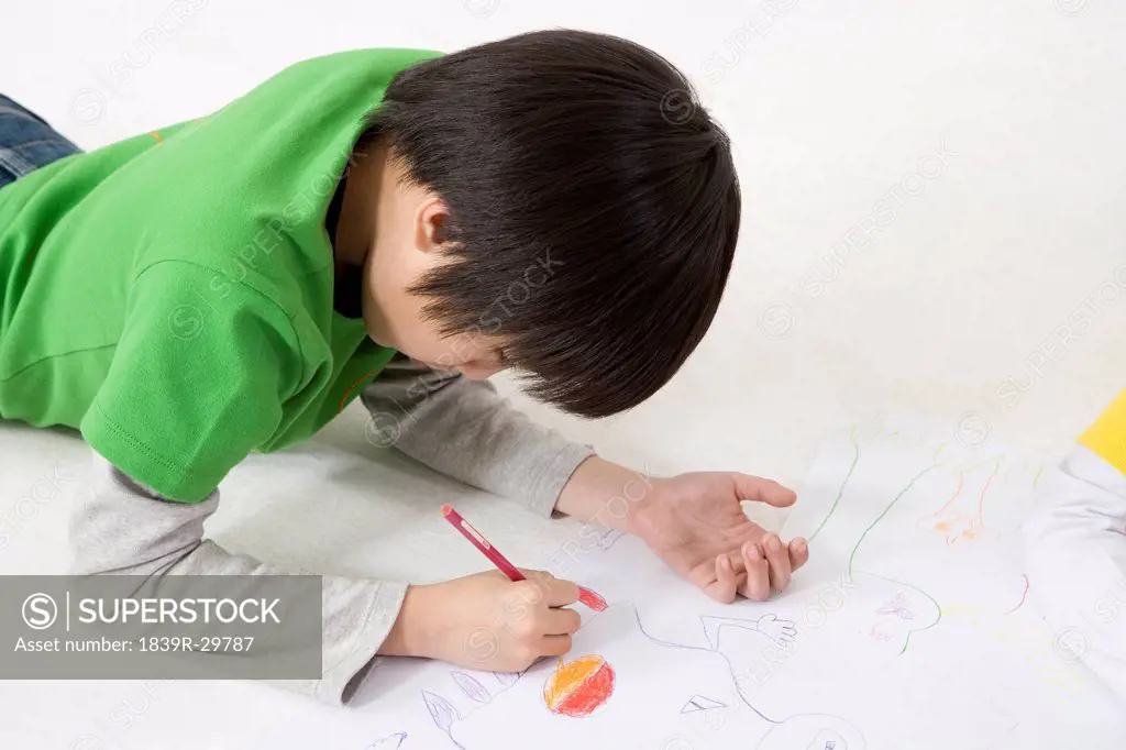 A young boy coloring while lying on the floor
