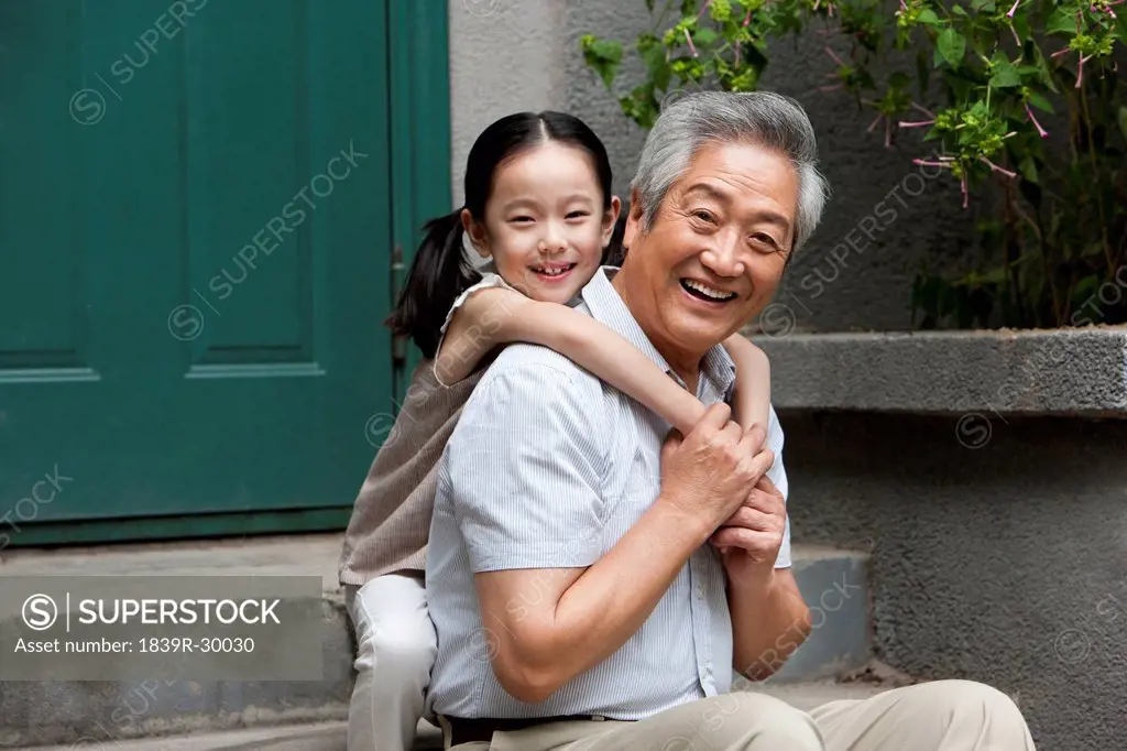 Chinese Grandfather and Grandaughter embracing on front stoop
