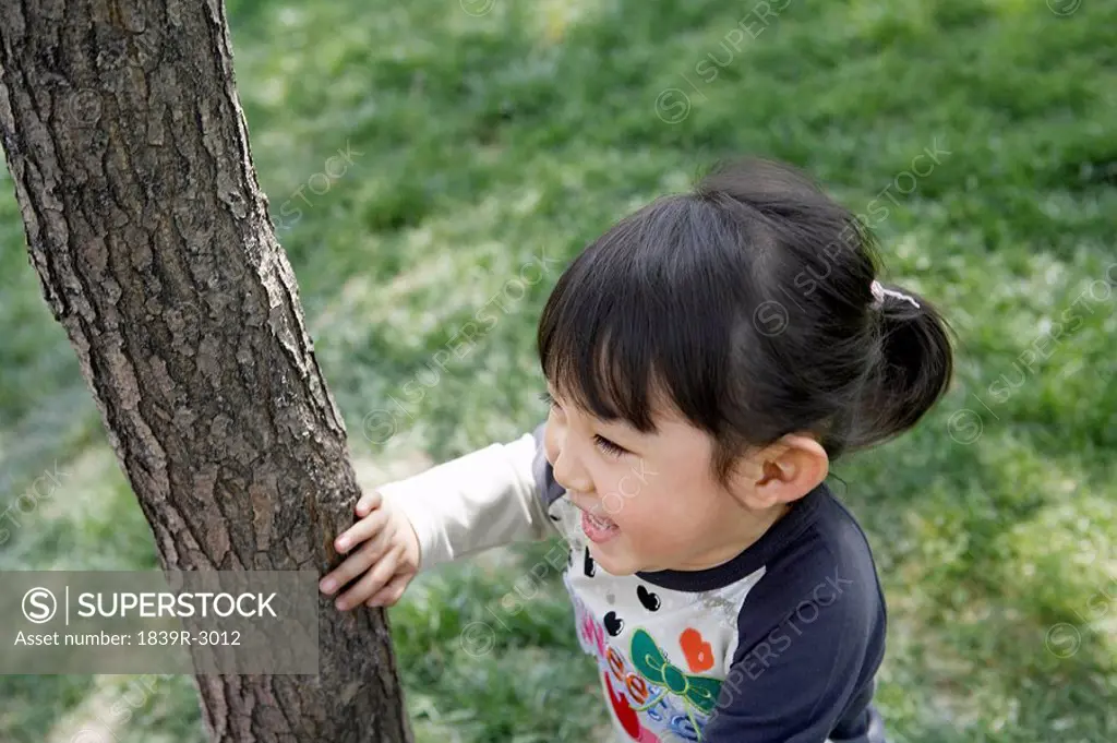 Young Girl Hiding Behind A Tree In The Park