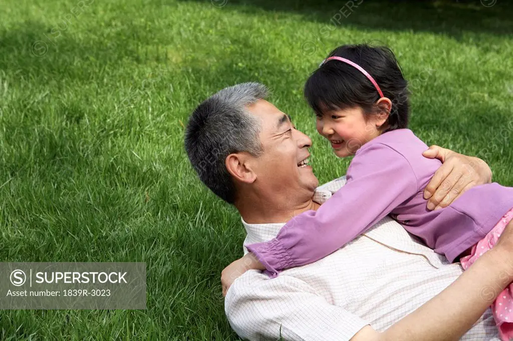 Grandfather And Granddaughter Hugging In The Park