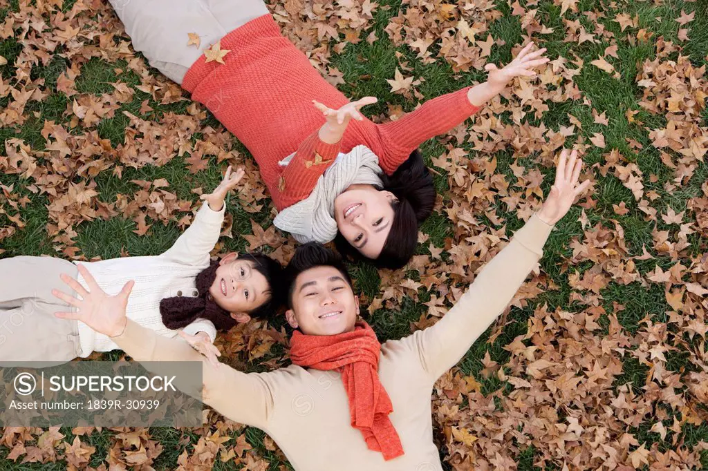 Young family lying on the grass surrounded by Autumn leaves