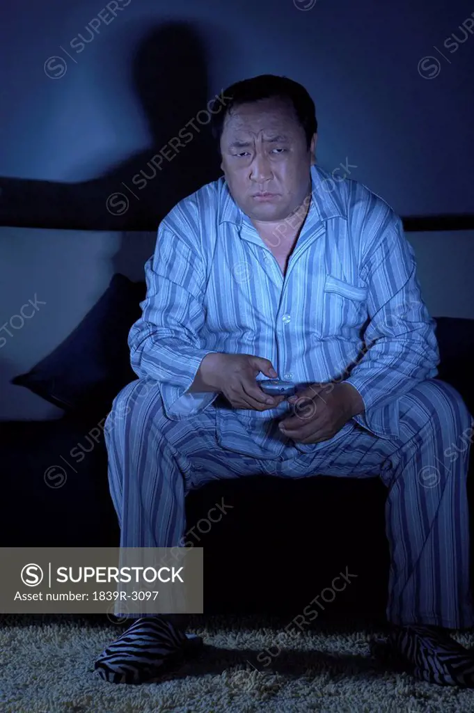 Man In Pajamas Sitting On Couch Watching Television