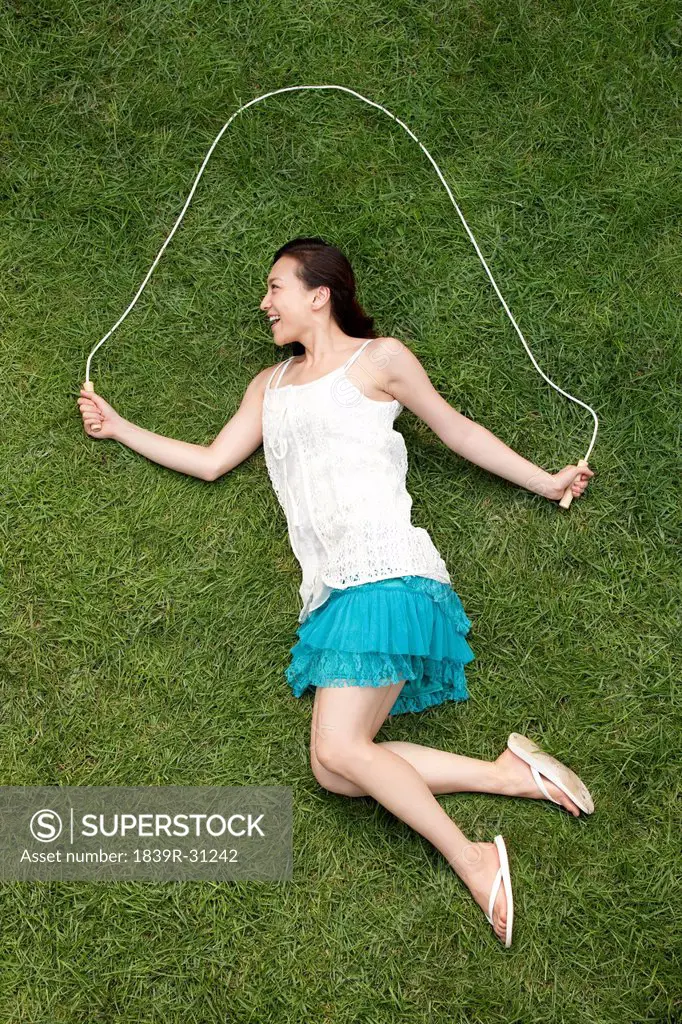 Creative young woman imitating jumping rope on meadow
