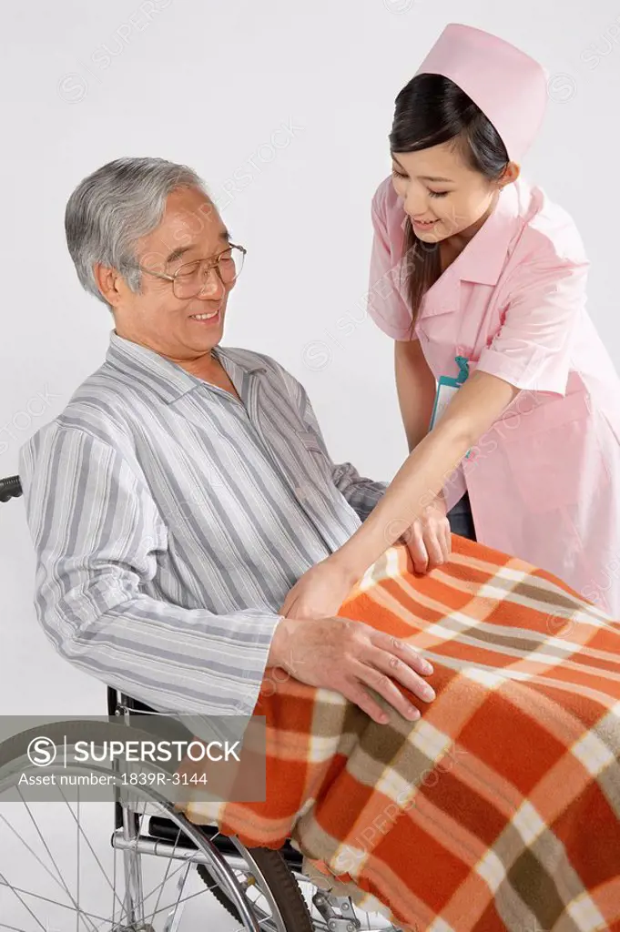 Nurse Fixing Blanket For Man In Wheelchair
