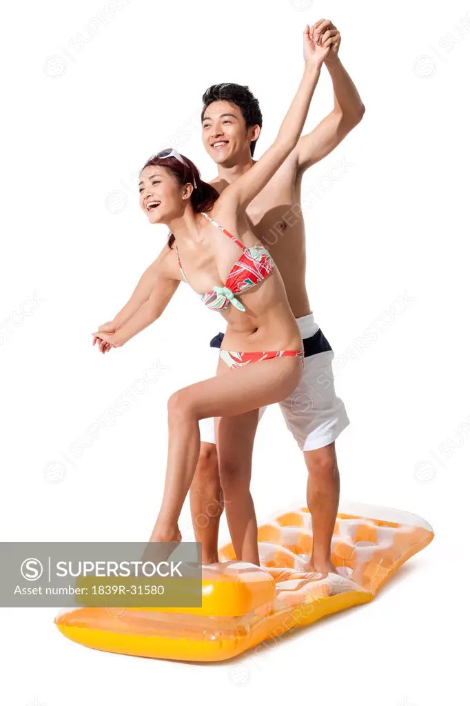 Young man and young woman in swimsuit having fun in air bed