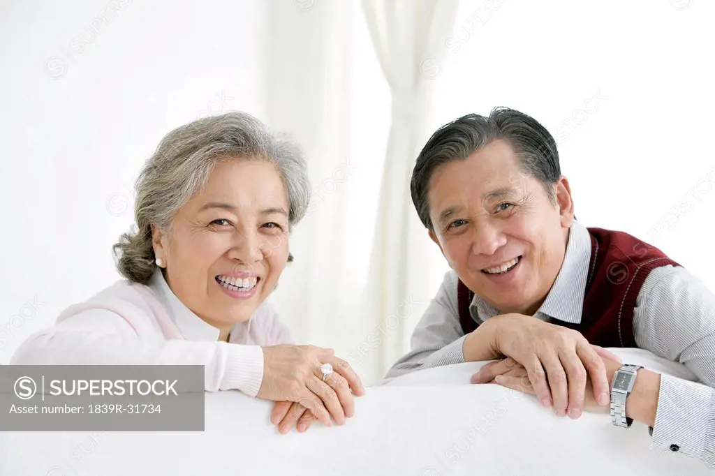 Senior Chinese couple turning around and smiling on the living room sofa