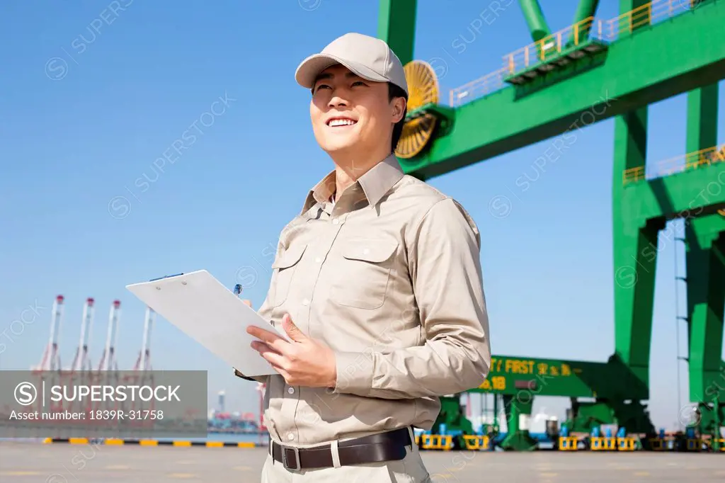 Male shipping industry worker with shipping dock and crane in the background
