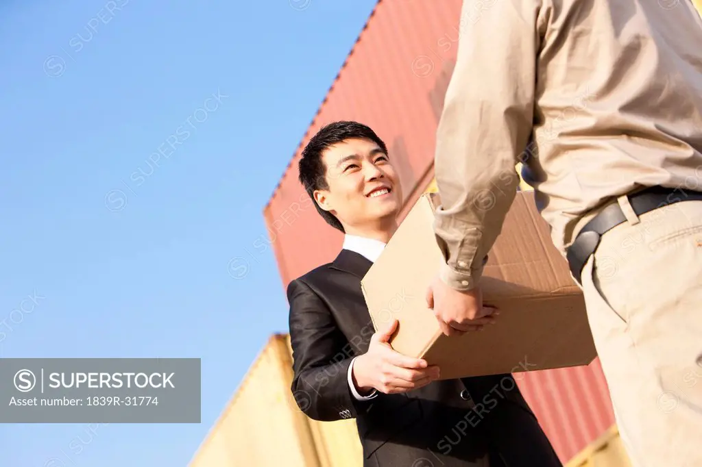 businessman and shipping industry worker giving and receiving a cardboard box