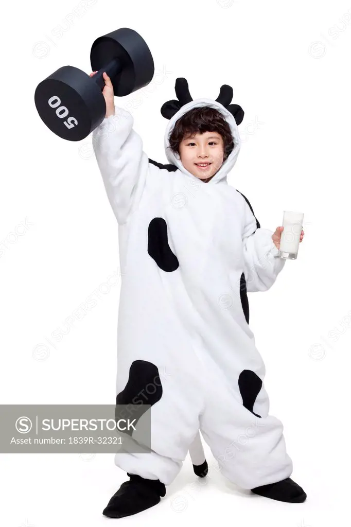 Cute boy in a cow costume with a glass of milk lifting a dumbbell