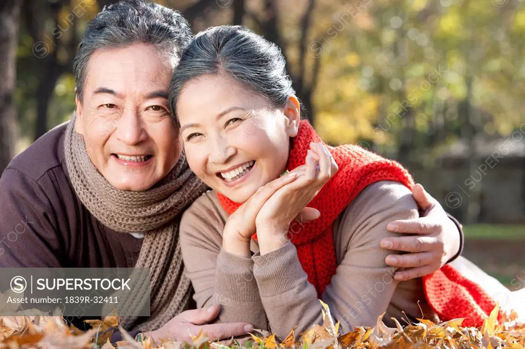 Senior couple lying on the grass surrounded by Autumn leaves