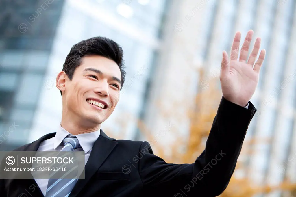 A businessman outside office buildings waving