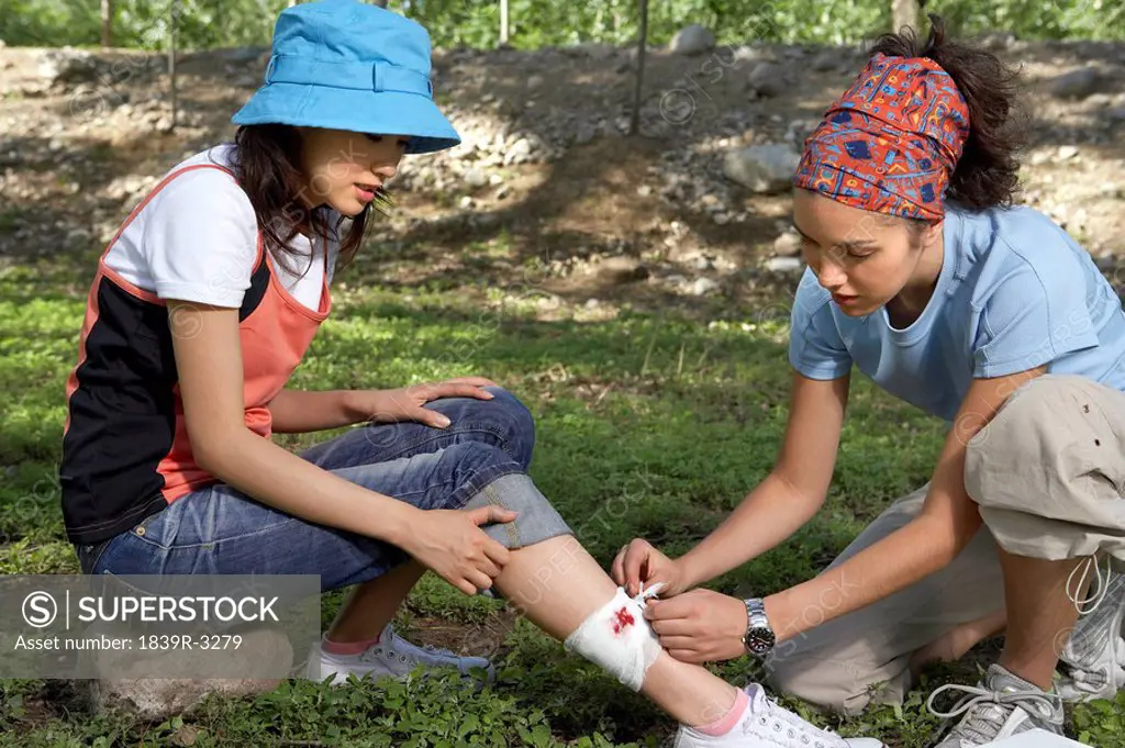 Girl Bandaging Friends Injured Leg