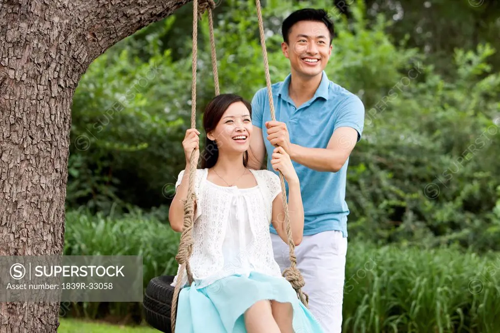Merry young couple playing on a swing
