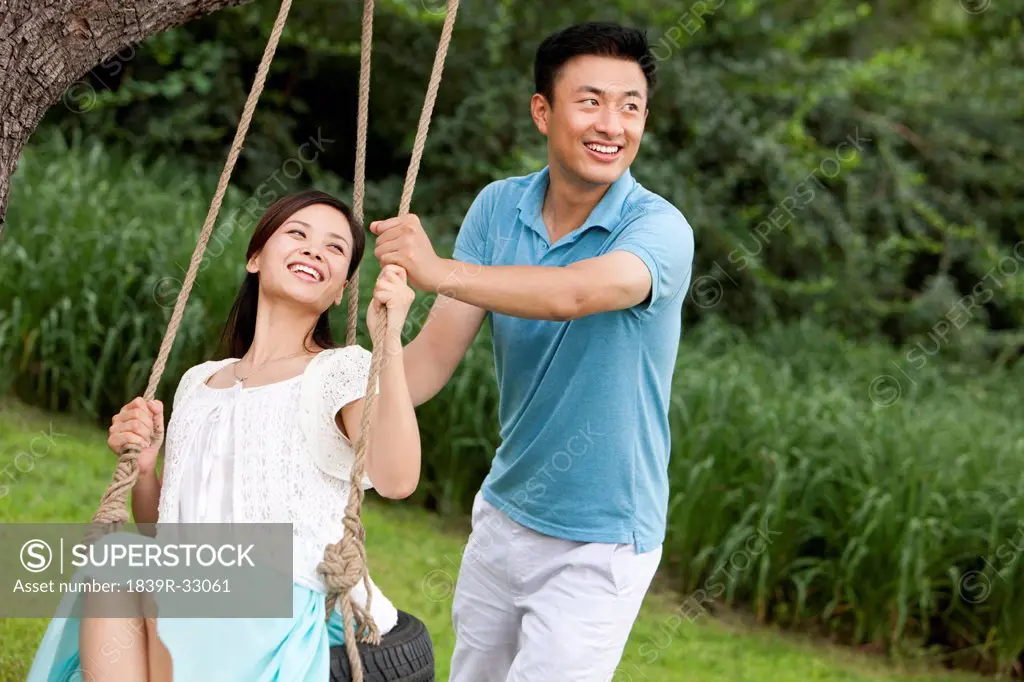 Joyful young couple playing on a swing