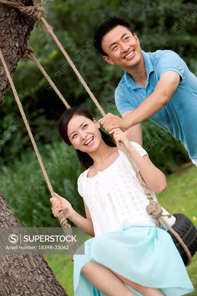 Joyful young couple playing on a swing
