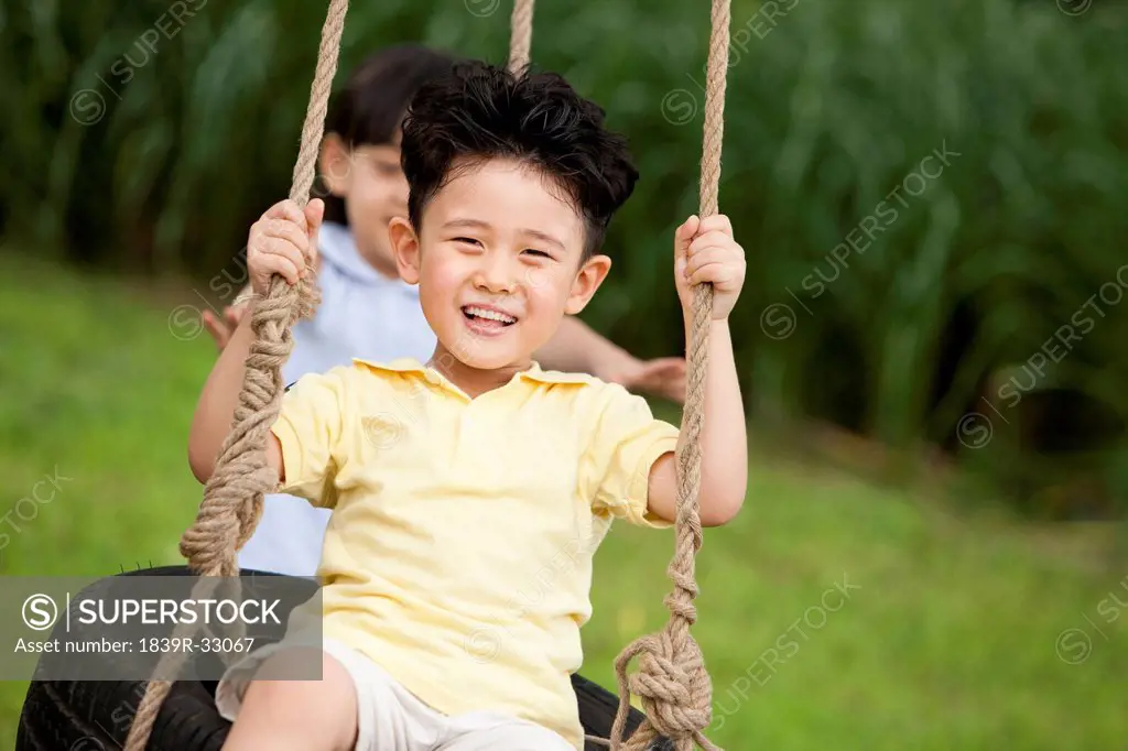 Excited boy playing on a swing with little girl behind