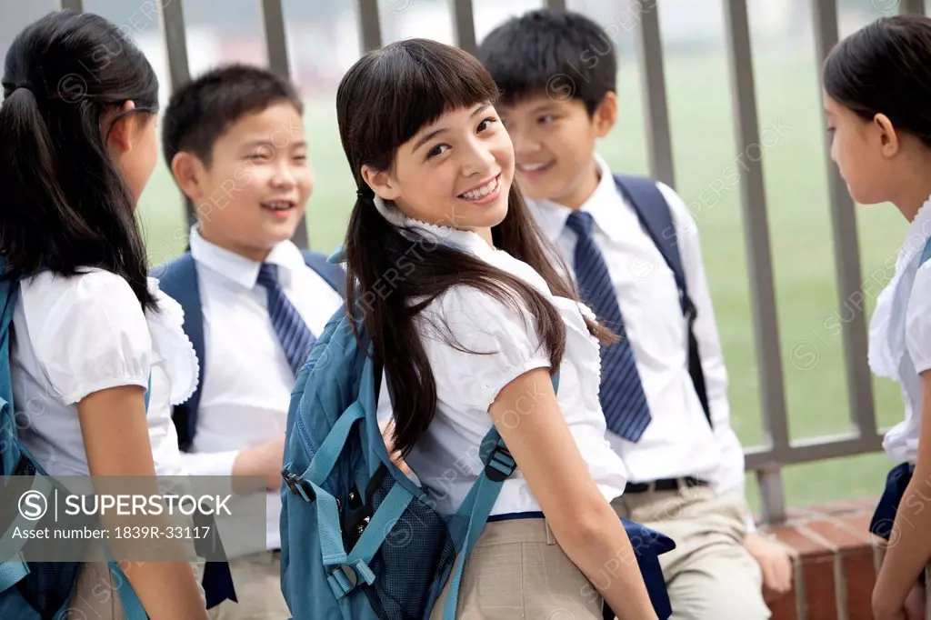 Happy schoolgirl in uniform with her friends outdoors