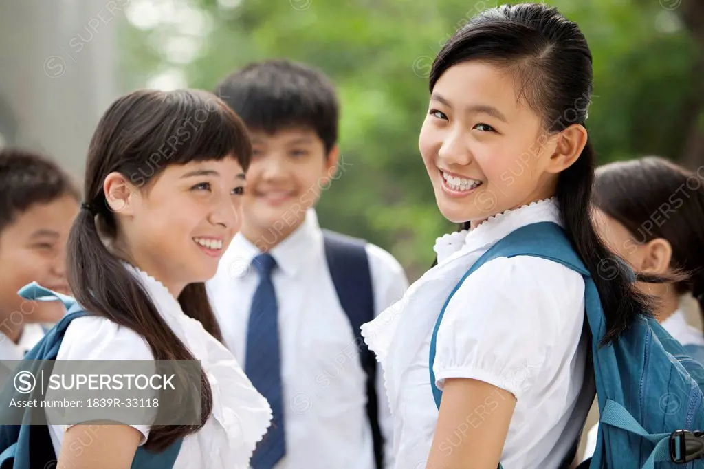 Happy schoolgirl in uniform with her friends outdoors