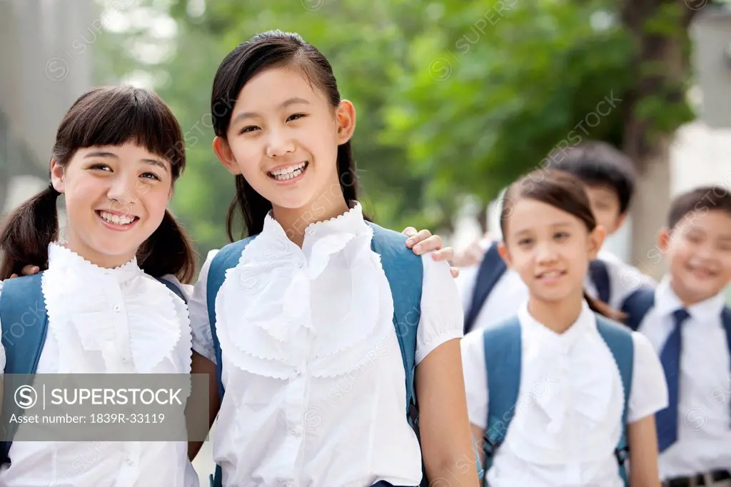 Happy schoolgirls in uniform with friends outdoors