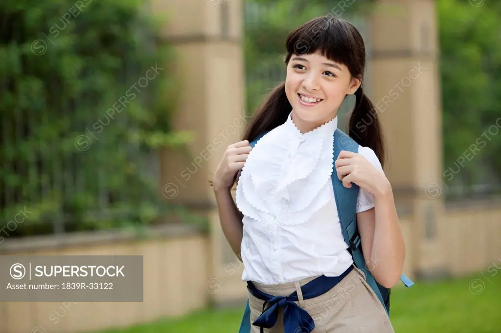 Cute schoolgirl in uniform carrying schoolbag on the back at school yard