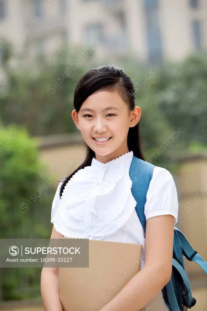 Lovely schoolgirl in uniform with book in hand at school yard
