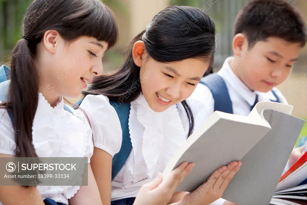 Cute schoolchildren in uniform reading books at school yard