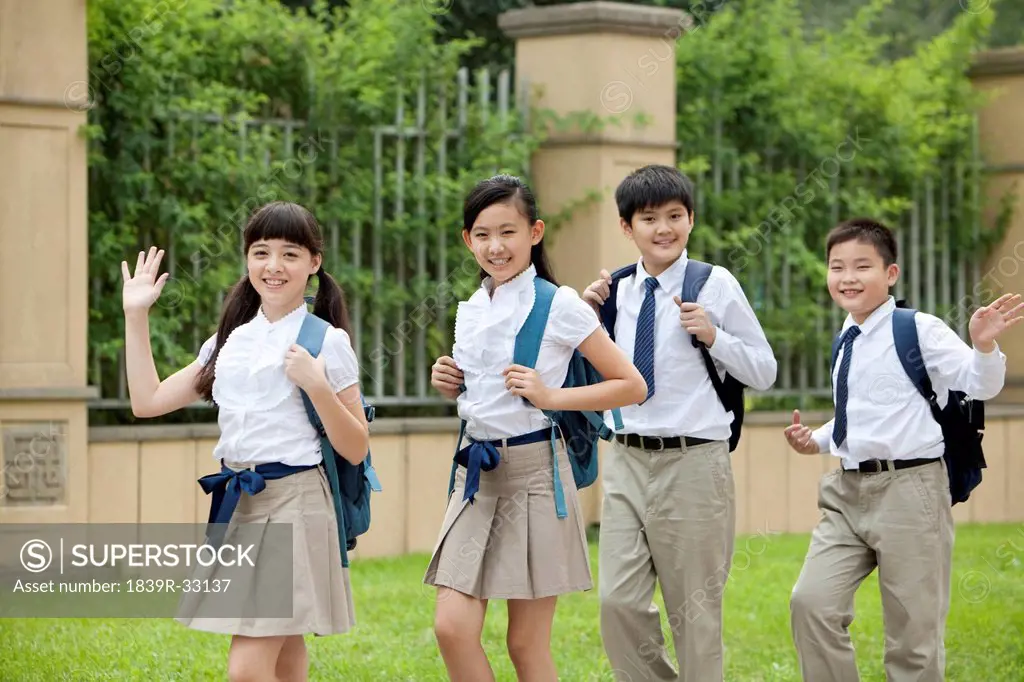 Cute schoolchildren in uniform waving at school yard