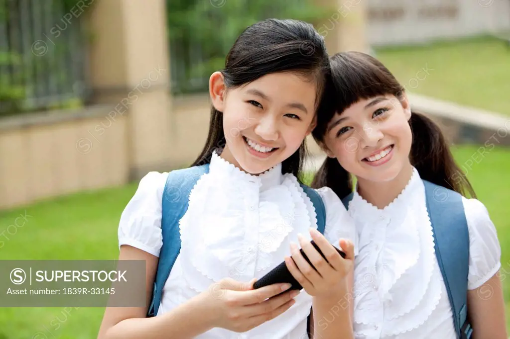 Excited schoolgirls in uniform with smart phone in school yard