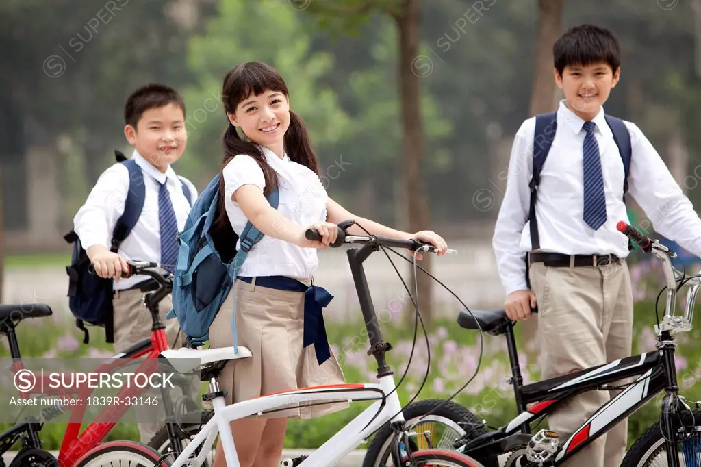 Happy schoolchildren in uniform with bicycles outdoors