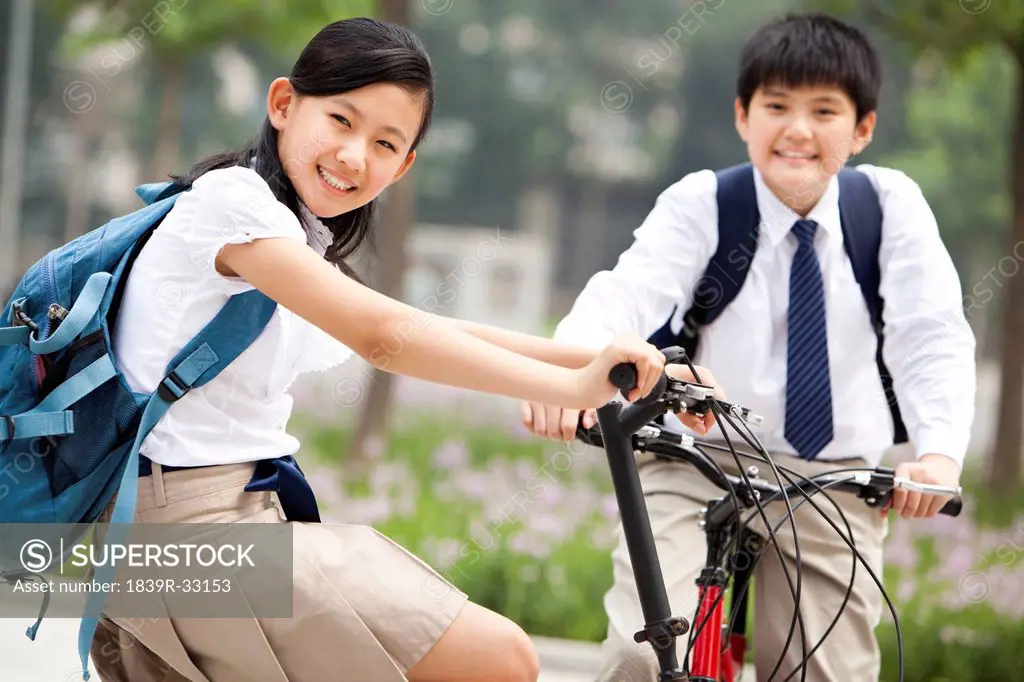 Happy schoolchildren in uniform with bicycles outdoors