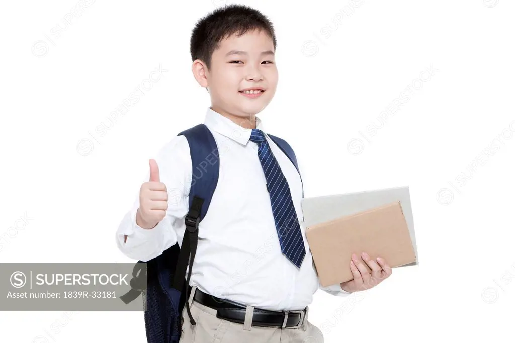 Portrait of confident schoolboy showing thumbs up with books