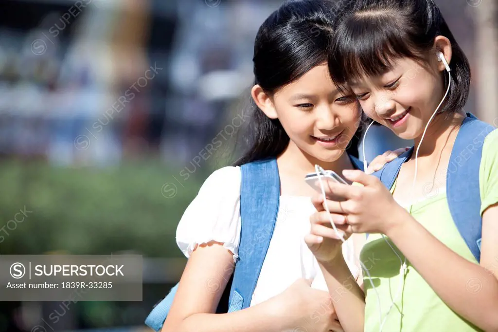 Schoolgirl playing smart phone with friend