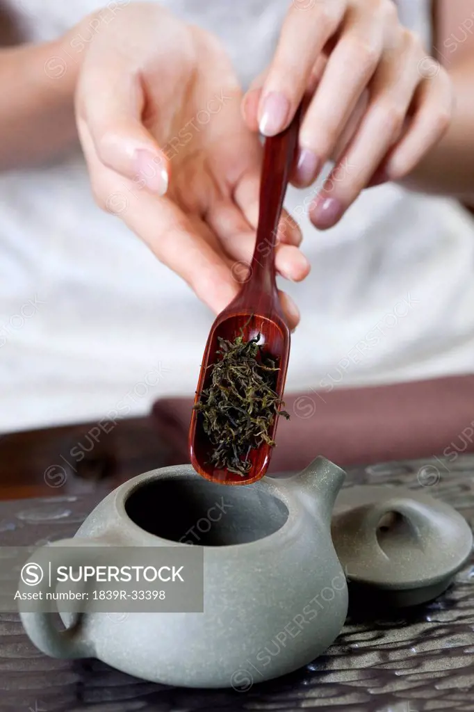 Female hand putting tea leaves into teapot