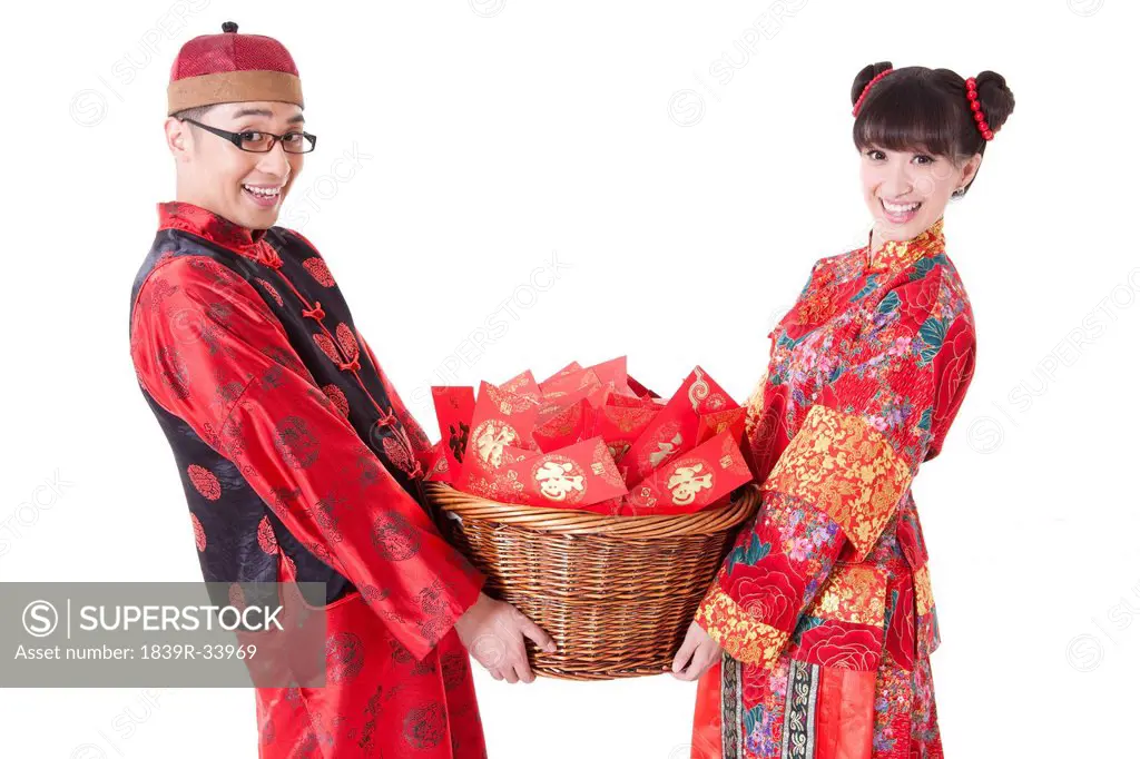 Cheerful young couple in Tang suit holding a basket of red pockets