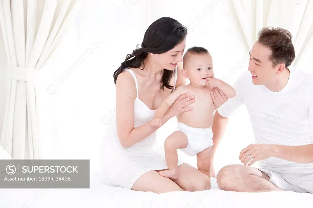 Happy young parents with cute baby in bedroom